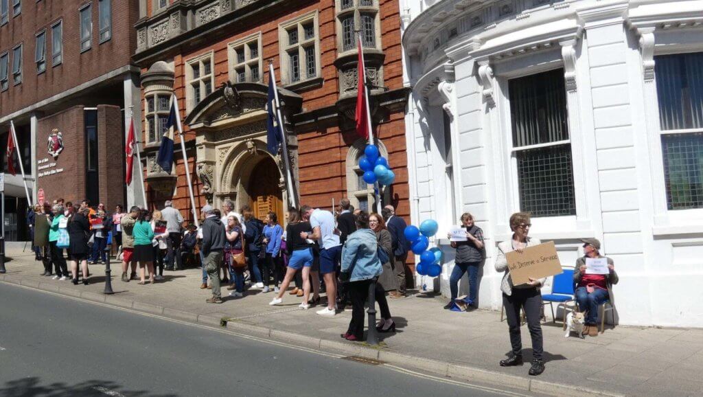 Protesters walk up and down sidewalk in front of parliament building