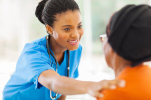 caring african-american medical nurse with hand on shoulder of a black senior patient in headwrap in office