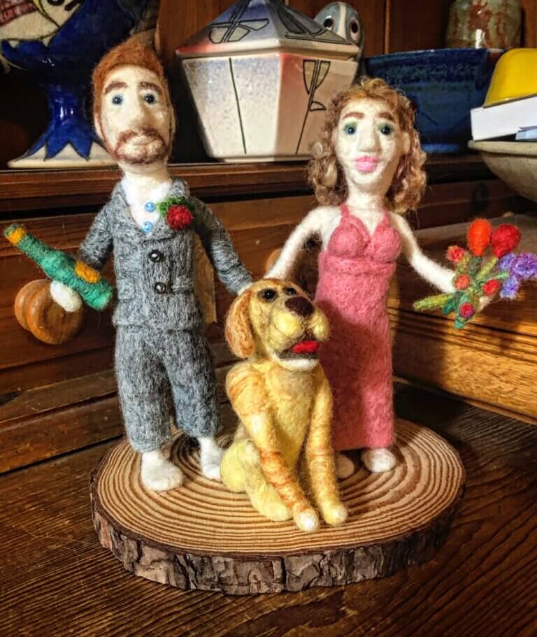 A statue of a couple holding flowers and wine in front of their golden retriever.