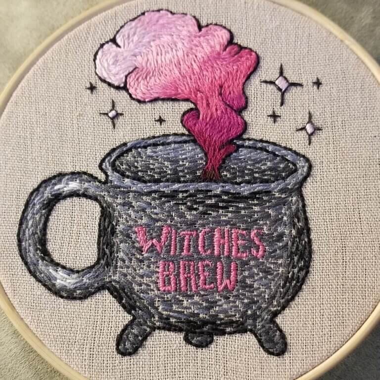 An embroidery of a cauldron that says witches brew and has pink ombre smoke coming out