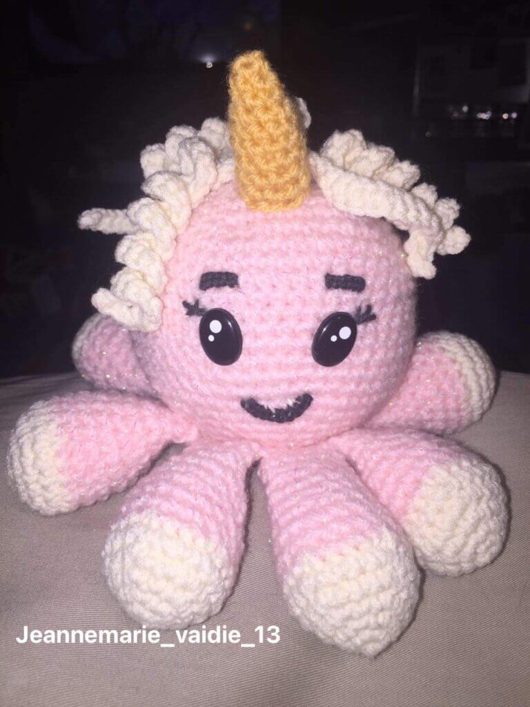A crocheted stuffed pink octopus with an ice cream cone unicorn horn