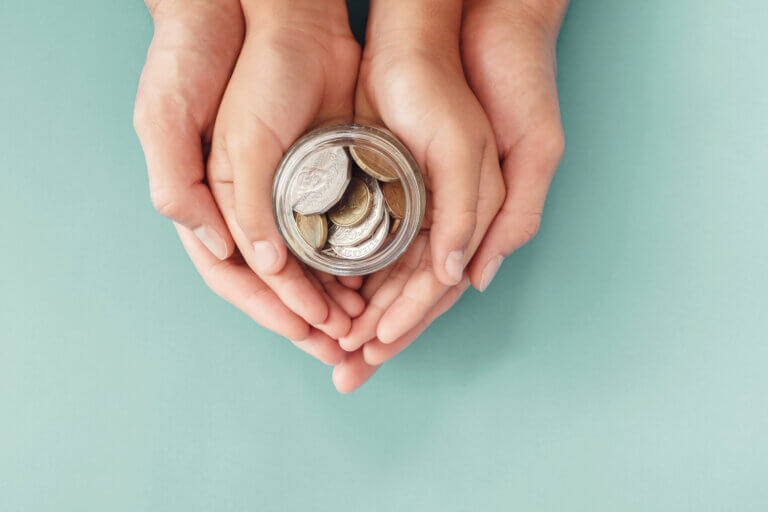 Two sets of hands joined together to hold a glass jar of coins.