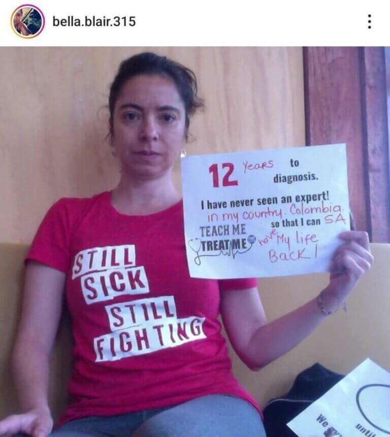 screenshot of an instgram post from bella.blair.315. They are wearing a red still sick still fighting shirt and holding a sign that says 12 years to diagnosis. I have never seen an expert in my country, Columbia. Teach me treat me, so that i can have my life back.